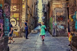 Das Foto zeigt Menschen in den Gassen Neapels, die mit bunten Graffiti verziert sind.