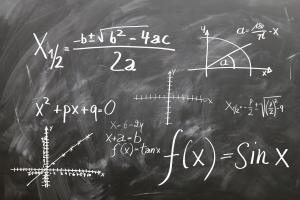 Mathematische Formeln und Schaubilder in weißer Kreide auf einer schwarzen Tafel.