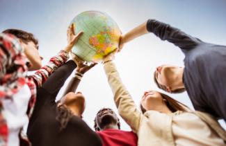 Junge Menschen unterschiedlicher Herkunft halten gemeinsam Weltkugel in die Höhe