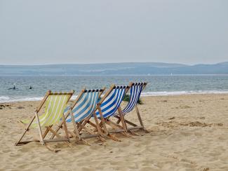 4 bunt gestreifte Klappliegestühle stehen am Strand vor Meereskulisse