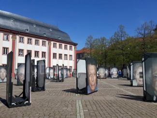 Aufnahme des Heidelberger Universitätsplatzes mit großformatigen Porträts von Überlebenden des Holocausts im Rahmen der Fotoausstellung „Gegen das Vergessen“ von Luigi Toscano; links im Bild die Alte Universität