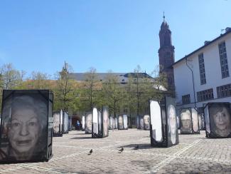 Aufnahme des Heidelberger Universitätsplatzes mit großformatigen Porträts von Überlebenden des Holocausts im Rahmen der Fotoausstellung „Gegen das Vergessen“ von Luigi Toscano; rechts im Bild die Neue Universität