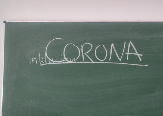 Auf einer grünen Tafel steht in großen Lettern unt unterstrichen das Wort „CORONA“; kleiner darunter und aufgrund der Nähe zu CORONA schlecht zu sehen das Wort „Inklusion“
