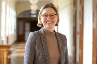 Das Bild zeigt Maria Friesen im Altbauflur der Pädagogischen Hochschule Heidelberg. Sie lächelt freundlich in die Kamera.