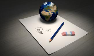 Eine Weltkugel steht auf einem Blatt, daneben ein Bleistift und ein Radiergummi. Auf dem Blatt sind eine Glühbirne und 3 Fragezeichen gezeichnet.