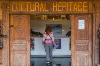 Auf einem hölzernen Portal ist der Schriftzug „CULTURAL HERITAGE“ zu lesen; durch die geöffnete Tür erkennt man eine Frau mit Rucksack vor einer Theke. | © Universität Heidelberg