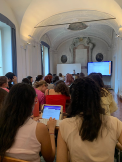 Studierende sitzen, z. T. mit Tablets, eng aneinandergedrängt in einem opulenten Altbau der Università degli Studi di Milano. Vorne sind Smart Screens zu erkennen.