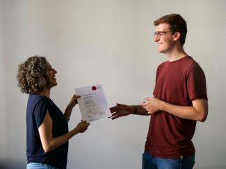 Ein Student nimmt von einer Mitarbeiterin des HSE-Prüfungsamts sein Zeugnis entgegen, beide lächeln.