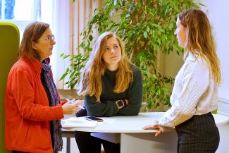 Drei Frauen unterschiedlichen Alters haben sich zu einem Beratungsgespräch um einen Stehtisch gruppiert.