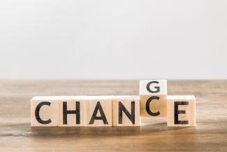 Buchstabenwürfel aus Holz bilden das Wort CHANCE. Das C ist gedreht, sodass auf der angrenzenden Seite ein G zu sehen ist. Botschaft: Change = Chance.