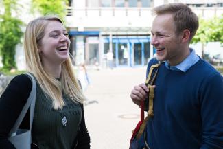Eine Studentin und ein Student fröhlich lachend vor einem Hochschulgebäude