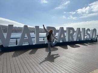 Eine junge Frau mit ausgebreiteten Armen vor den großen VALPARAÍSO-Lettern am Meer.