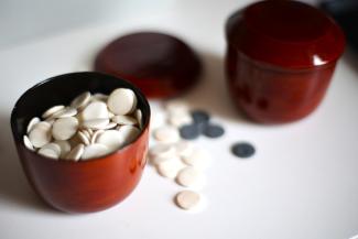 Auf einem Tisch stehen zwei mit weißen und schwarzen, runden Spielsteinen gefüllte rote Becher.