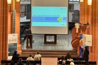 Dr. Dennis Dietz bei seinem Vortrag in der Akademischen Mittagspause am Pult der Peterskirche. Hinter ihm die Vortragsfolie..