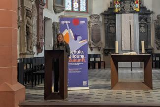 Prof. Dr. Susann Schäfer bei ihrem Vortrag in der Akademischen Mittagspause am Pult der Peterskirche. Hinter ihr das Roll-up zur Akademischen Mittagspause.
