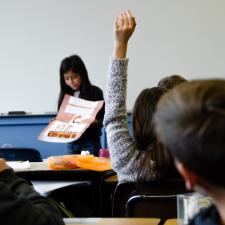 Ein dunkelhaariges Mädchen präsentiert im Unterricht ein Plakat; rechts im Vordergrund weitere Mitschüler:innen, eine meldet sich. | Bild: Taylor Wilcox | Unsplash
