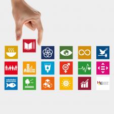 Eine Hand setzt zwischen bunte Kacheln, auf denen Icons zu den 7 Nachhaltigkeits-Zielen (SDGs) abgebildet sind, die Kachel mit dem Buch-Icon, das für hochwertige Bildung steht. | Quelle: 17ziele.de