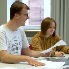 Ein Student und eine Studentin arbeiten mit aufgeklapptem Laptop gemeinsam am Schreibttisch