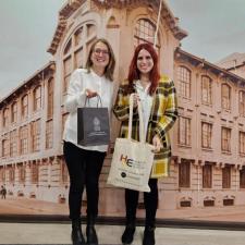 Dr. Lena Sowada und Dr. Ivania Yáñez vor einem Bild mit dem Gebäude der PUCV. In den Händen halten beide eine Tasche der jeweils anderen Hochschule.