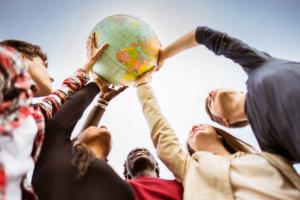 Junge Menschen unterschiedlicher Herkunft halten gemeinsam Weltkugel in die Höhe