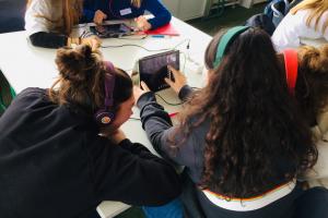 Schülerinnen mit Kopfhörern beugen sich über Tablet
