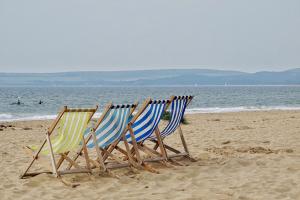 4 bunt gestreifte Klappliegestühle stehen am Strand vor Meereskulisse