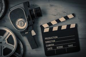Das Bild zeigt in Graustufen eine Filmrolle, eine Handkamera und eine Regieklappe. | Bild: Canva