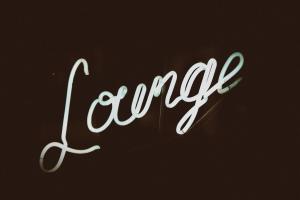 Weiß leuchtender LED-Schriftzug „Lounge“ auf dunkelbraunem Grund | Bild: Unsplash/Jon Tyson