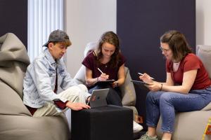 3 Studierende sitzen auf Sitzsäcken und arbeiten auf laptops bzw. Tablets.