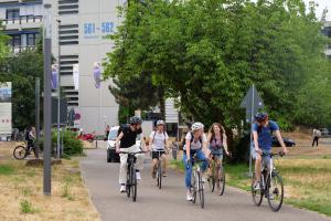 5 Studierende radeln durch den Campus im Neuenheimer Feld, hinter ihnen der Neubau der Pädagogischen Hochschule.