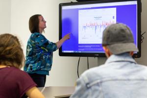 Dr. Nicole Aeschbach zeigt an einem Smartboard eine Grafik zu Temperaturanomalien; im Vordergrund sind Studierende zu erkennen.