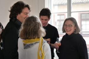 Eine lachende Petra Deger im Gespräch mit Michael Haus, Christiane Wienand, Sebastian Mahner; in ihrer Hand ein Sektglas.