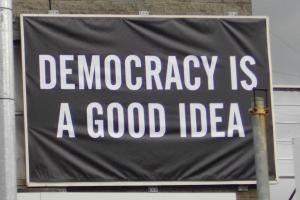 Auf einem schwarzen Banner steht in weißen Lettern DEMOCRACY IS A GOOD IDEA.