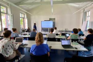 Im Konferenzraum der HSE stellen Dr. Thomas Renkert und Dr. Florian Nieser an einem Smartboard das Projekt ParzivAI vor. Im Vordergrund sind Teilnehmer:innen mit Laptops zu sehen.