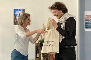 Christiane Wienand überreicht Michael Haus vor dem Gabentisch eine HSE-Tasche mit Aufdruck "You'll never walk alone", beide lachen.