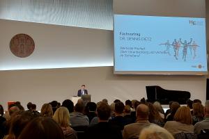 Dr. Dennis Dietz bei seinem Fachvortrag „Wertvolle Freiheit. Über Verantwortung und Vertrauen im Schulberuf“ am Rednerpult. Neben ihm die Leinwand mit Vortragstitel, vor ihm Publikum.