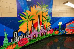 Das Bild zeigt ein in tropischen Farben gehaltenes, handgemaltes New York-Wandbild in einem gekachelten High-School-Flur.