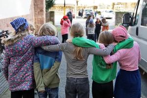 Das Bild zeigt von hinten 5 Schüler:innen, die Arm in Arm in einem Schulhof stehen. Im Hintergrund weitere Schüler:innen.