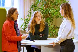 Drei Frauen unterschiedlichen Alters haben sich zu einem Beratungsgespräch um einen Stehtisch gruppiert.