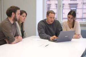Eine Gruppe junger Menschen gruppiert um ein Laptop an einem Stehtisch