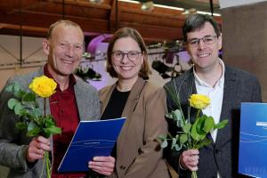 Die Preisträger Prof. Dr. Manfred Seidenfuß (links) und Andreas Spiziali (rechts) halten eine gelbe Rose und ihre Urkunde in der Hand. In ihrer Mitte die Laudatorin Prof. Dr. Marita Friesen.