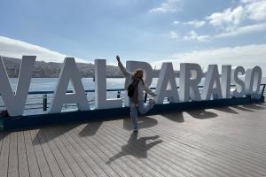 Eine junge Frau mit ausgebreiteten Armen vor den großen VALPARAÍSO-Lettern am Meer.