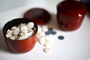 Auf einem Tisch stehen zwei mit weißen und schwarzen, runden Spielsteinen gefüllte rote Becher.