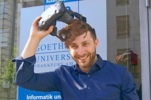 Prof. Dr. Andreas Dengel zieht sich eine VR-Brille vom Kopf, im Hintergrund ein Schild der Goethe-Universität.