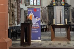 Prof. Dr. Susann Schäfer bei ihrem Vortrag in der Akademischen Mittagspause am Pult der Peterskirche. Hinter ihr das Roll-up zur Akademischen Mittagspause.