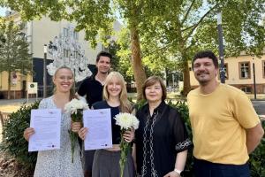 Die Absolvent:innen Julia Düchting und Laura Schweikert halten auf dem grünen Campus Bergheim ihre Zertifikate und Blumen in den Händen.  Hinter ihnen Geschäftsführer Dr. Sebastian Mahner, rechts Prof. Dr. Havva Engin und Dr. Daniel Vetter