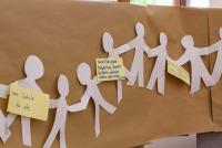 An einer langen Pinnwand hängt eine Menschenkette aus Papier, darauf gepinnt Gedanken der Teilnehmenden zu gleichberechtigter Teilhabe. Bild: © Heidelberg School of Education | Vanessa Bender
