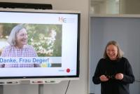 Petra Deger lachend neben einem Smartboard, auf dem ihr Foto mit dem Schriftzug „Danke, Frau Deger!“ zu lesen ist.