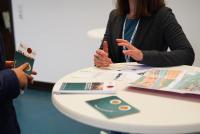 An einem mit Informaterialien ausgelegten Tisch berät eine HSE-Mitarbeiterin eine:n Studieninteressierte:n. Die Gesichter sind nicht zu sehen.