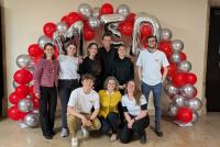 'Das Orgateam der Absolvent:innenfeier bestehend aus HSE-Prüfungsamt, weiteren HSE-Mitarbeiterinnen und Hilfskräften unter einem Luftballon-Bogen in Silber und Weiß. Oben formen Buchstaben-Ballons "M ED".'